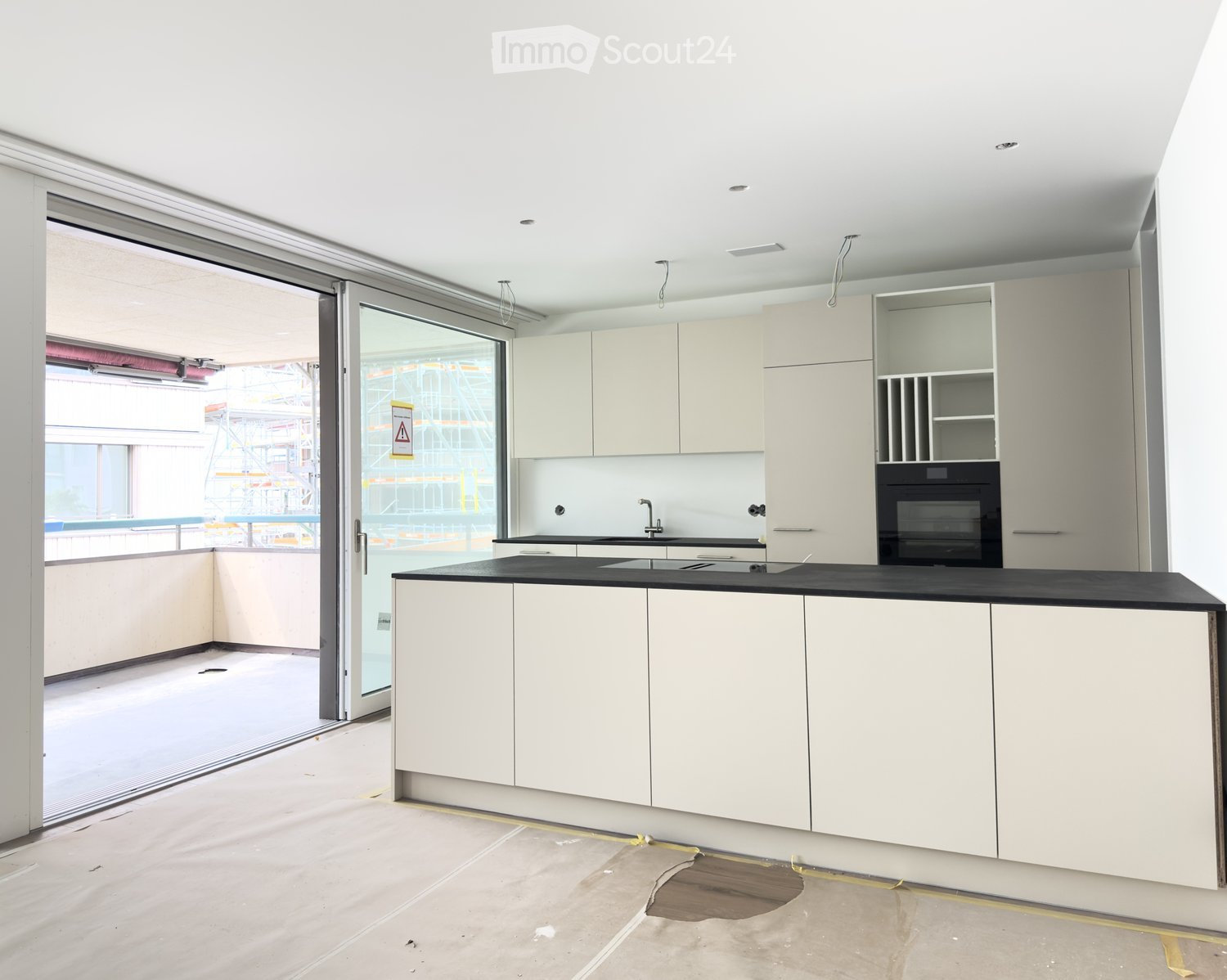 Modern kitchen with white cabinets, black countertop, sink, faucet, and built-in oven. Large sliding glass door provides access to an outdoor area.