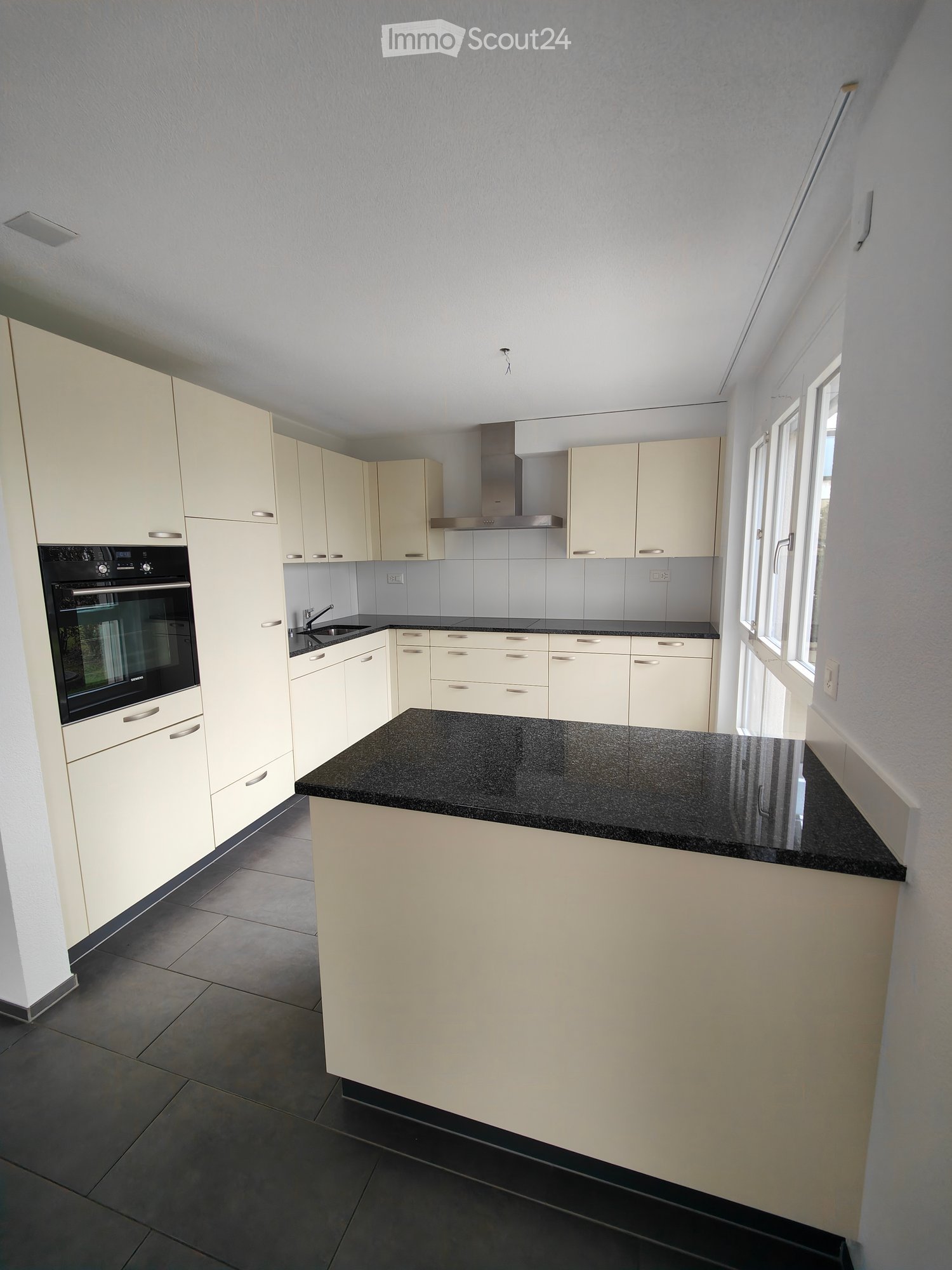 Modern kitchen with light-colored cabinets, black granite countertops, and stainless steel appliances including an oven and range hood.