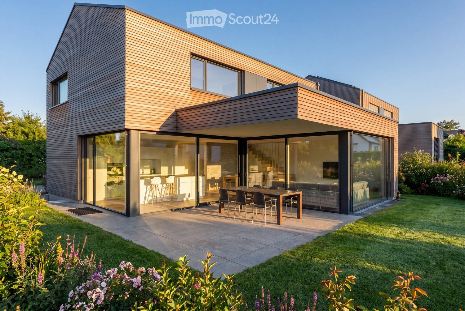 Modern two-story house with wooden exterior, large glass sliding doors, and a spacious patio area with a dining table and chairs.