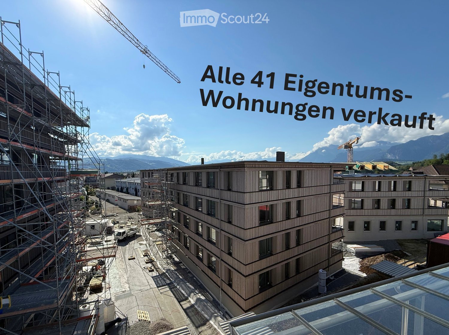 A modern multi-story building under construction with scaffolding, cranes, and a clear blue sky in the background.