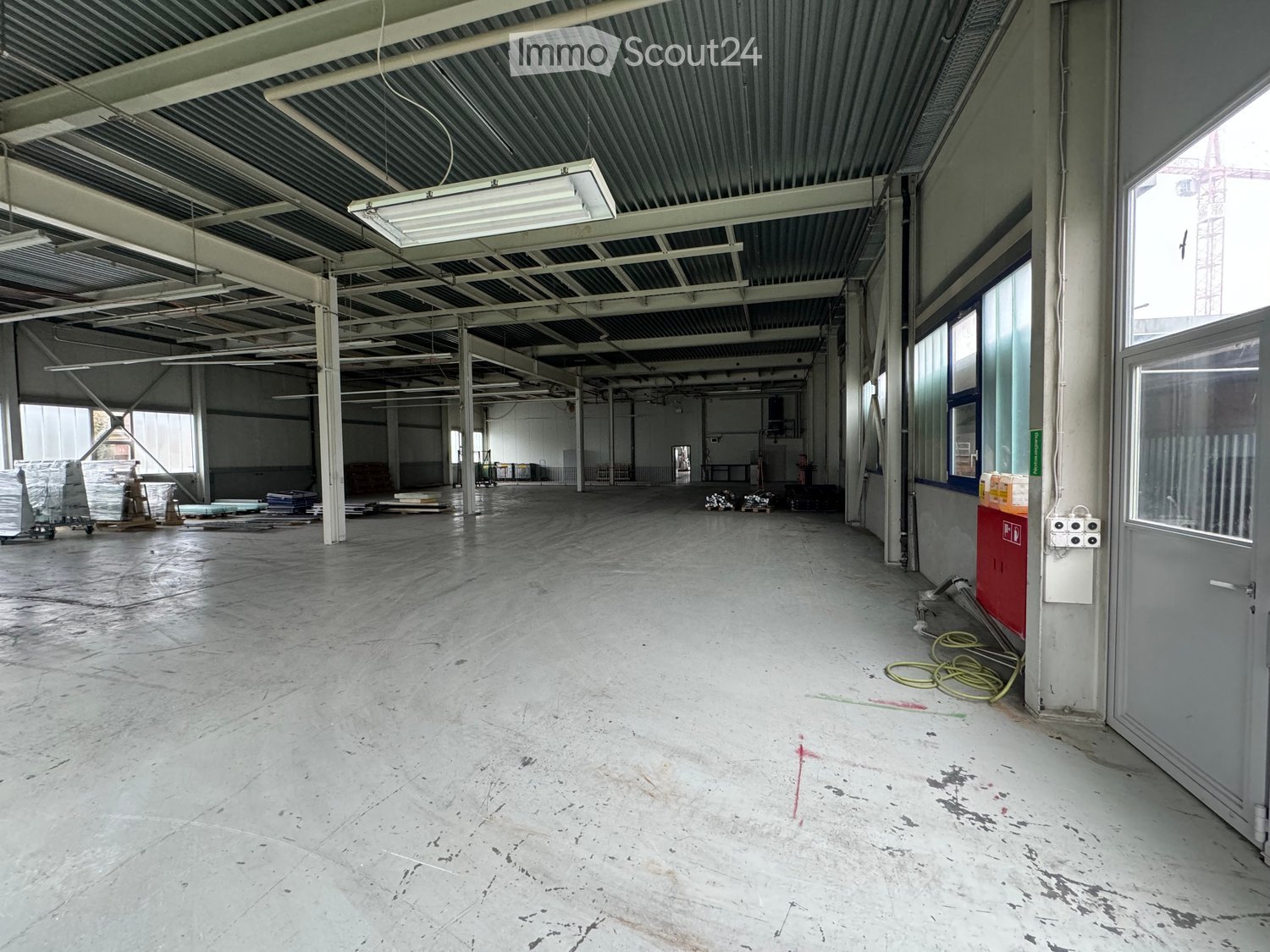 large open space, metal ceiling, fluorescent lighting, wide aisles, windows on the far wall, red pillar at the corner, door at the end