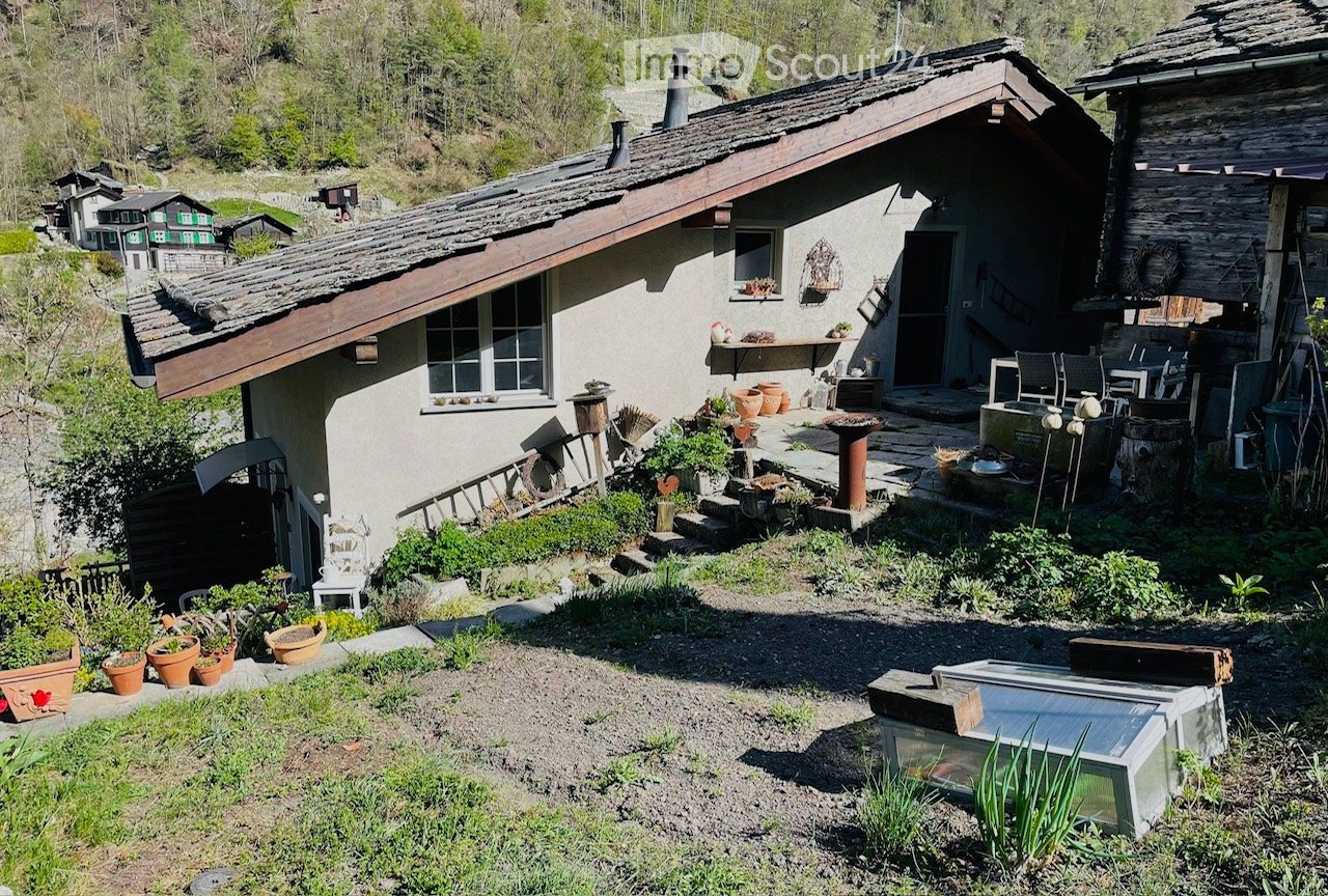 A rustic garden area with a small house, potted plants, outdoor furniture, and a stone pathway.