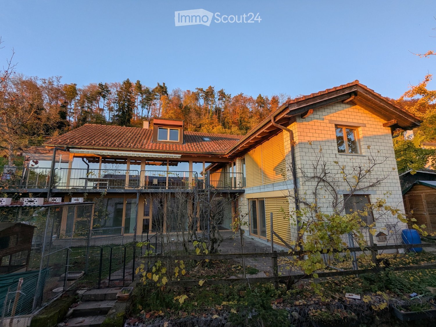 3 story house, yellow exterior, red tiles, large balcony, garden, forest backdrop
