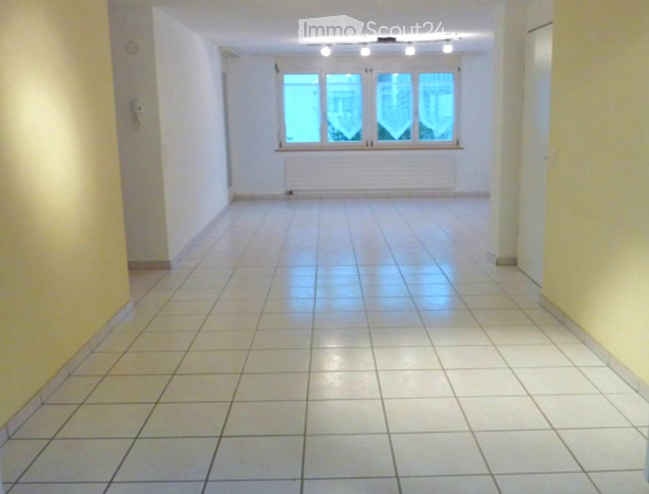 Empty hallway with tiled floor, white walls, and a large window at the end.