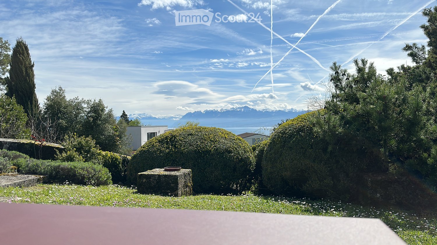 Garden with well-maintained hedges, a stone bench, and a scenic view of mountains and a lake in the background.