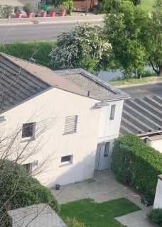 Single-story white house with grey roof, multiple windows, and a small garden area with green lawn and trimmed hedges.