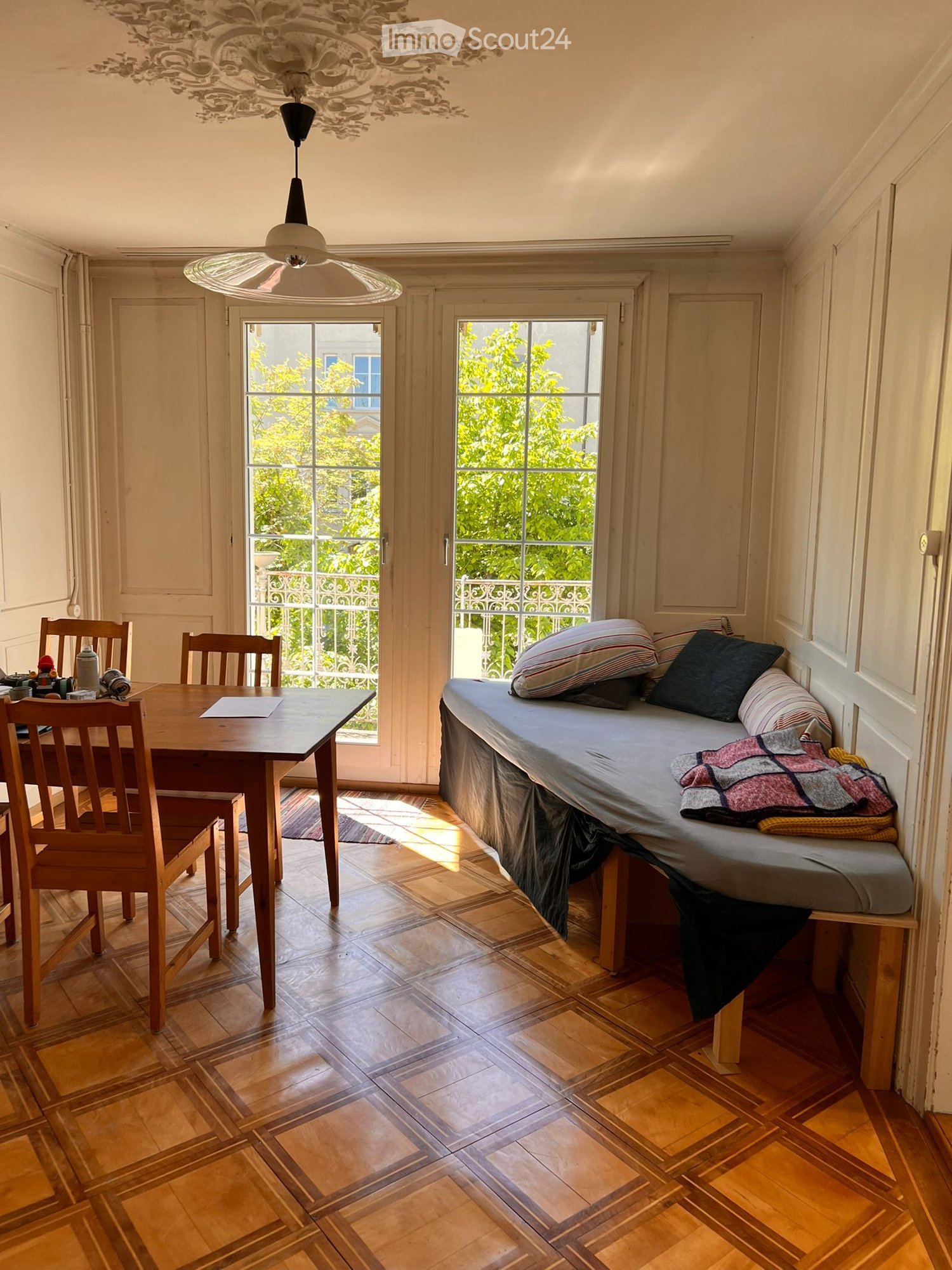 Cozy room with a daybed, wooden dining table, chairs, and a view of greenery through large windows.