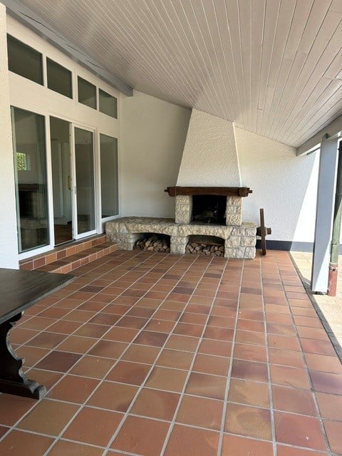 Outdoor patio with terracotta tiles, a stone fireplace, and a wooden table. Large glass doors lead to the interior.