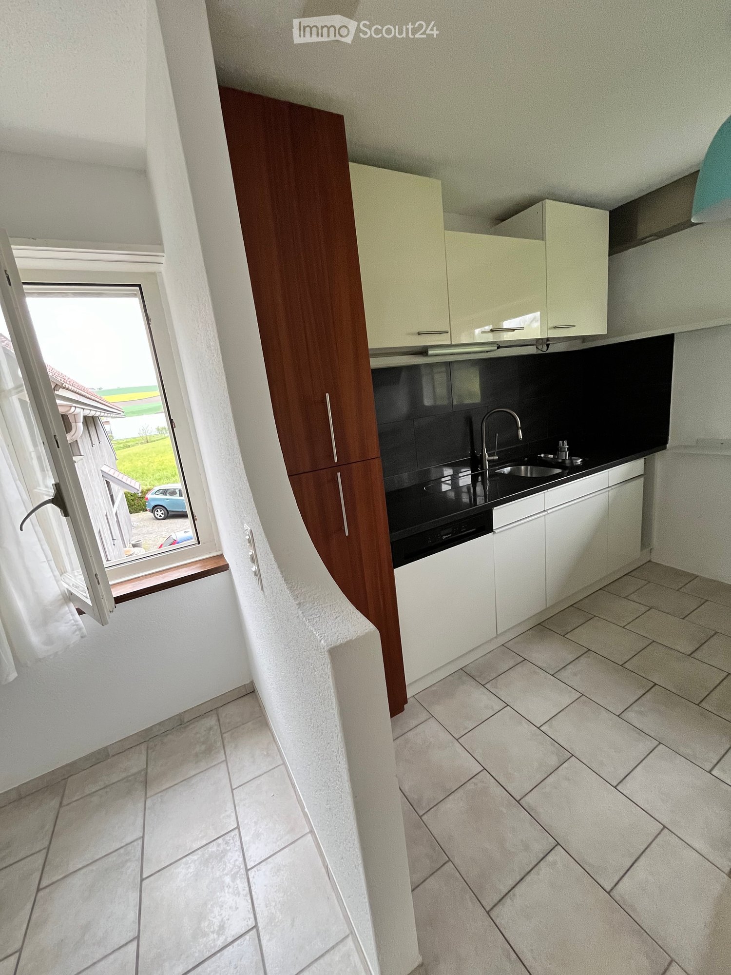 Modern kitchen with white and cream cabinets, black countertops, and a tiled floor. Features a sink with a modern faucet and an oven below the countertop.