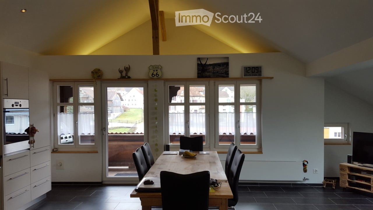 Bright, open room with a dining table and chairs, modern kitchen cabinetry, and large windows overlooking a yard.
