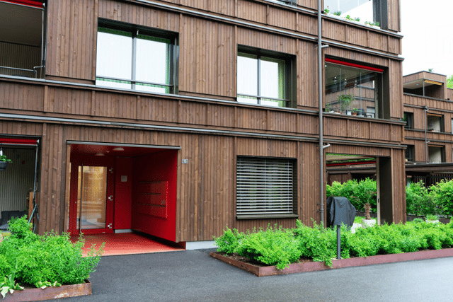 Modern multi-story building with wooden facade, large windows, and a red garage entrance.