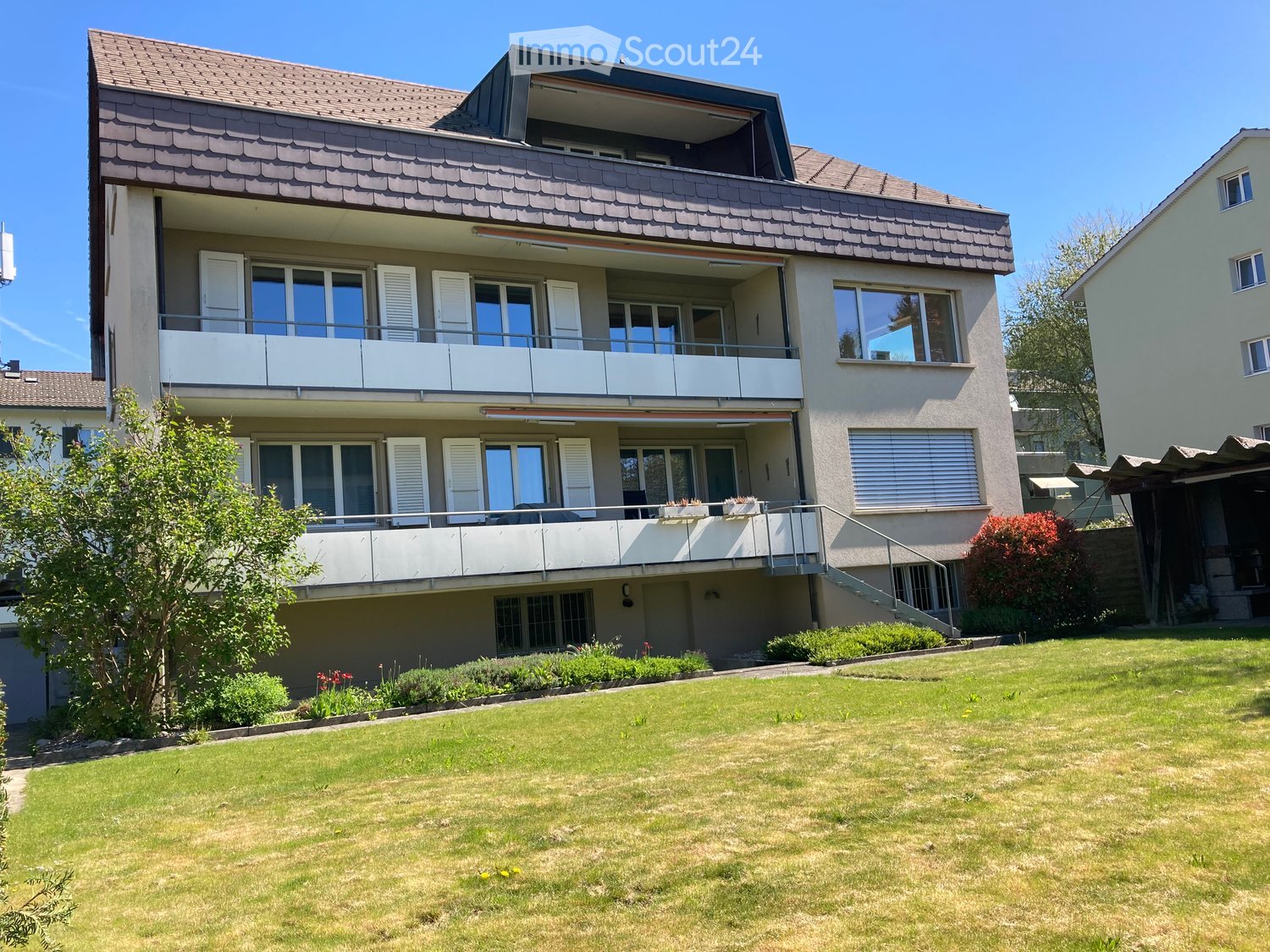 Two-story house with balconies, large windows, and a well-maintained lawn in front.