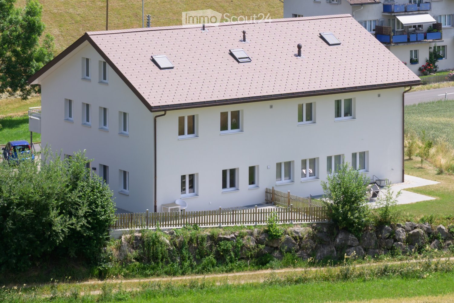 Two-story white house with multiple windows, solar panels on the roof, and a small fenced garden area with outdoor furniture.
