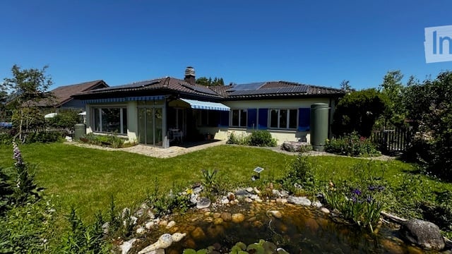 Single-family house with a well-maintained garden, pond, and patio area. The house features a blue shutters and a striped awning over the entrance.