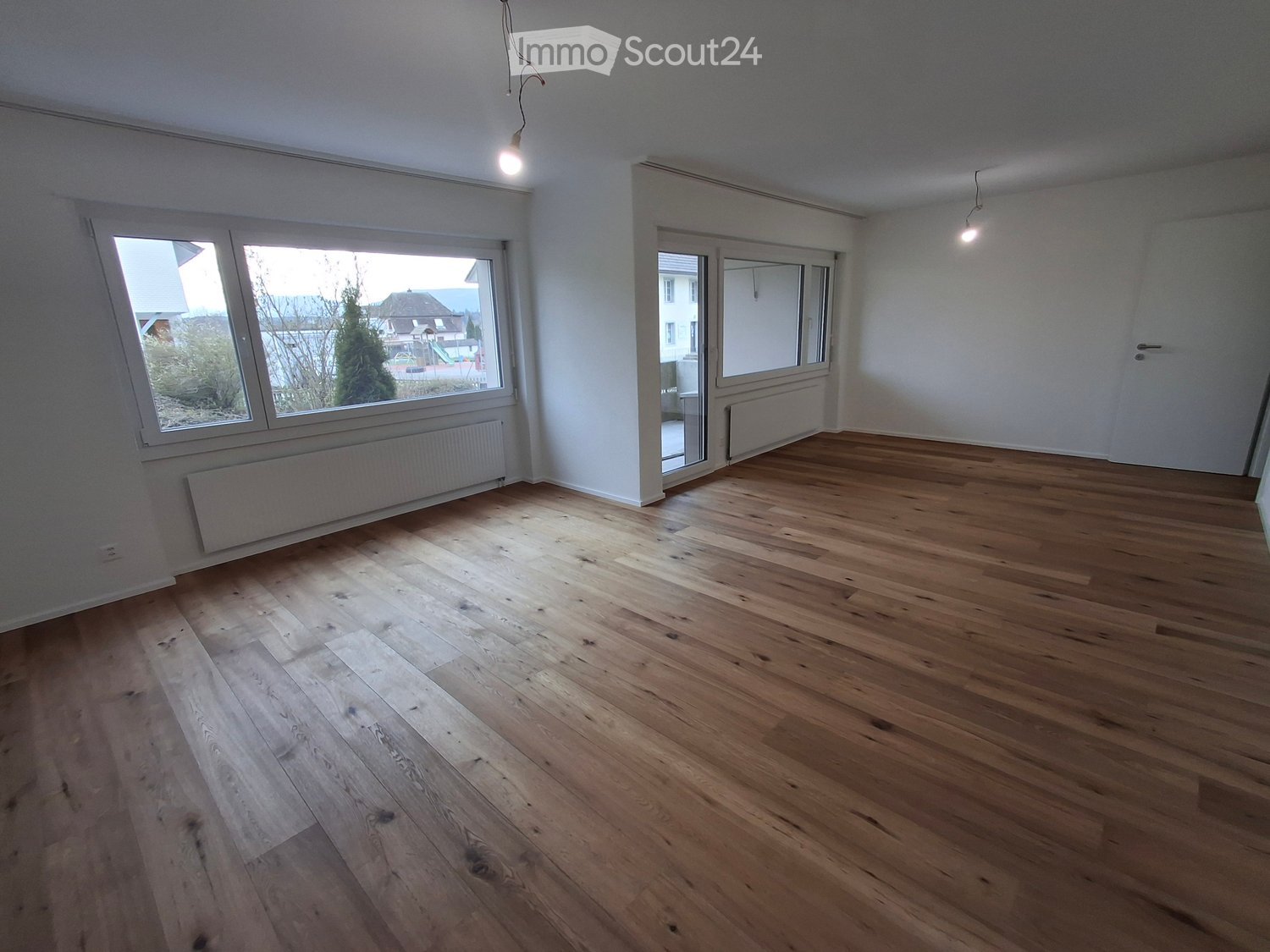 Empty room with hardwood floors, large windows, white walls, and ceiling lights