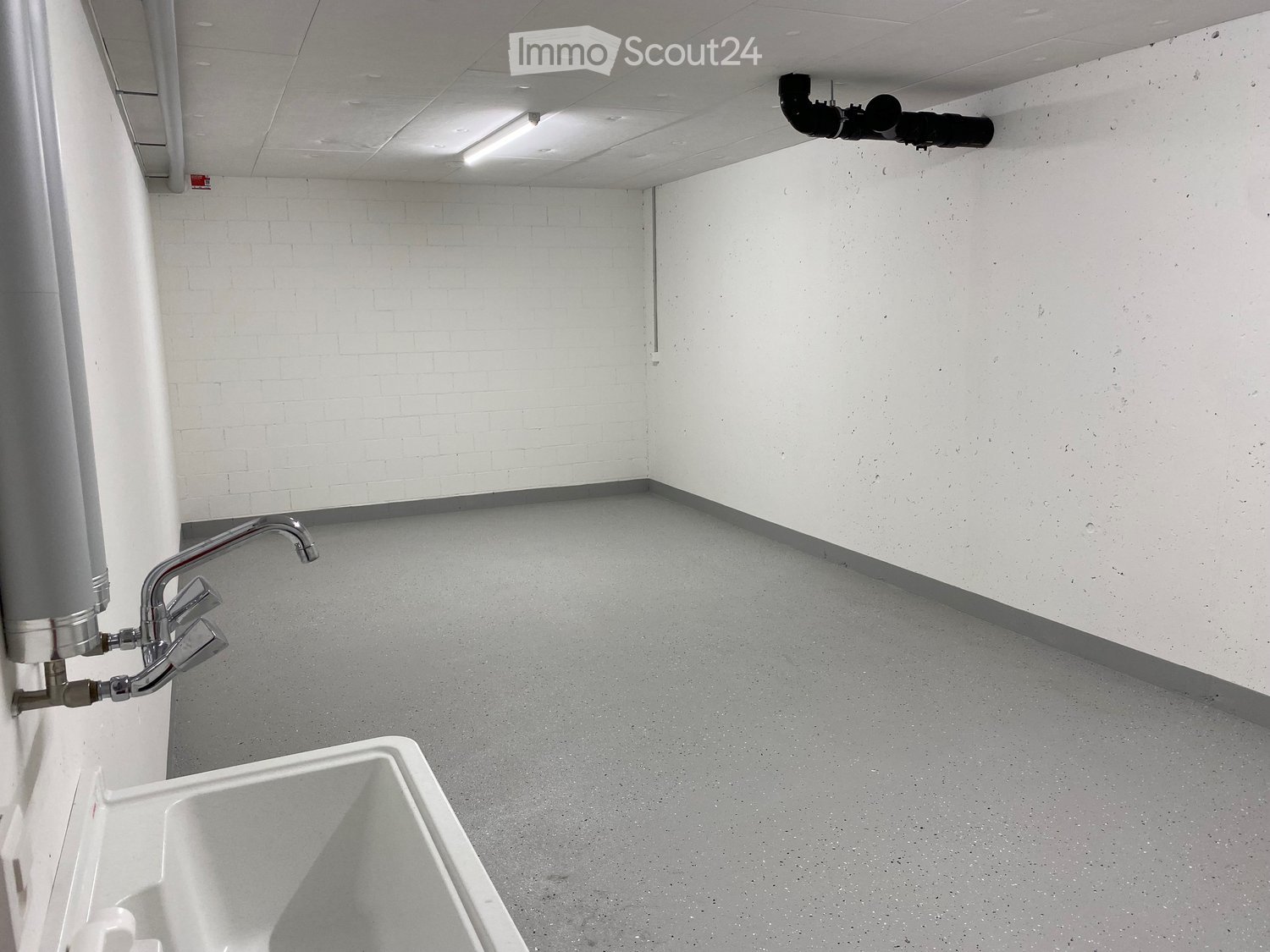 Empty room with white brick walls, grey concrete floor, a sink, and a water heater unit on the wall.