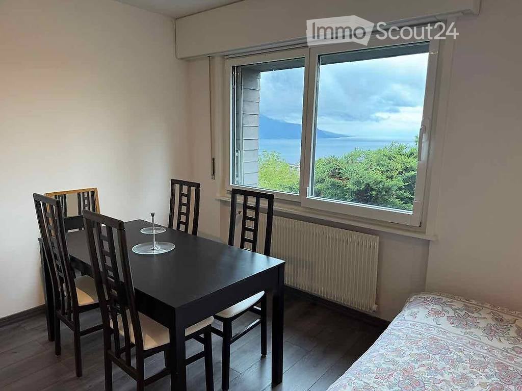 Dining area with a black dining table, six chairs, and a cup on the table. Large windows offer a scenic view of the lake and mountains.