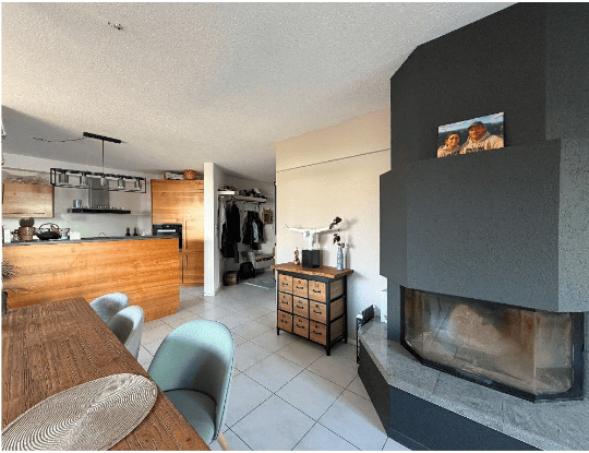 Open-plan living and dining area with a modern kitchen island, dining table, chairs, and a fireplace with a TV mounted above it.
