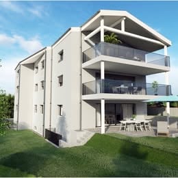 Modern multi-story residential building with balconies, green lawn, and outdoor furniture.