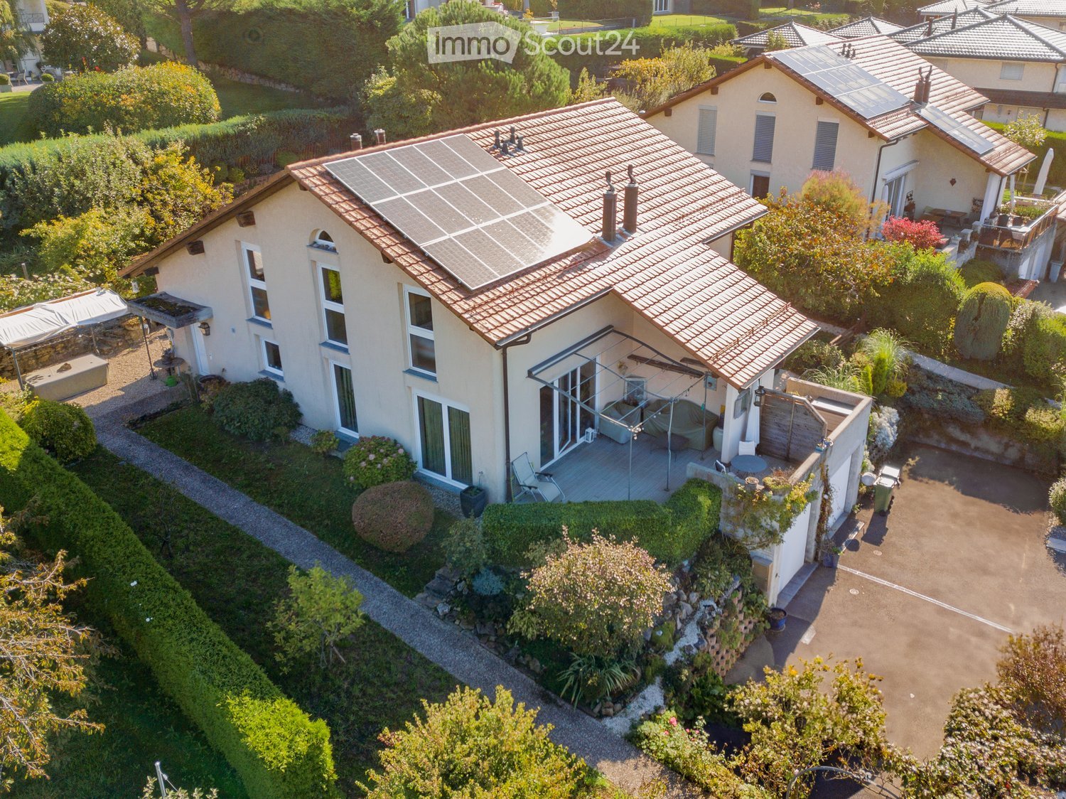 Aerial view of a modern house with solar panels on the roof, surrounded by a well-maintained garden.
