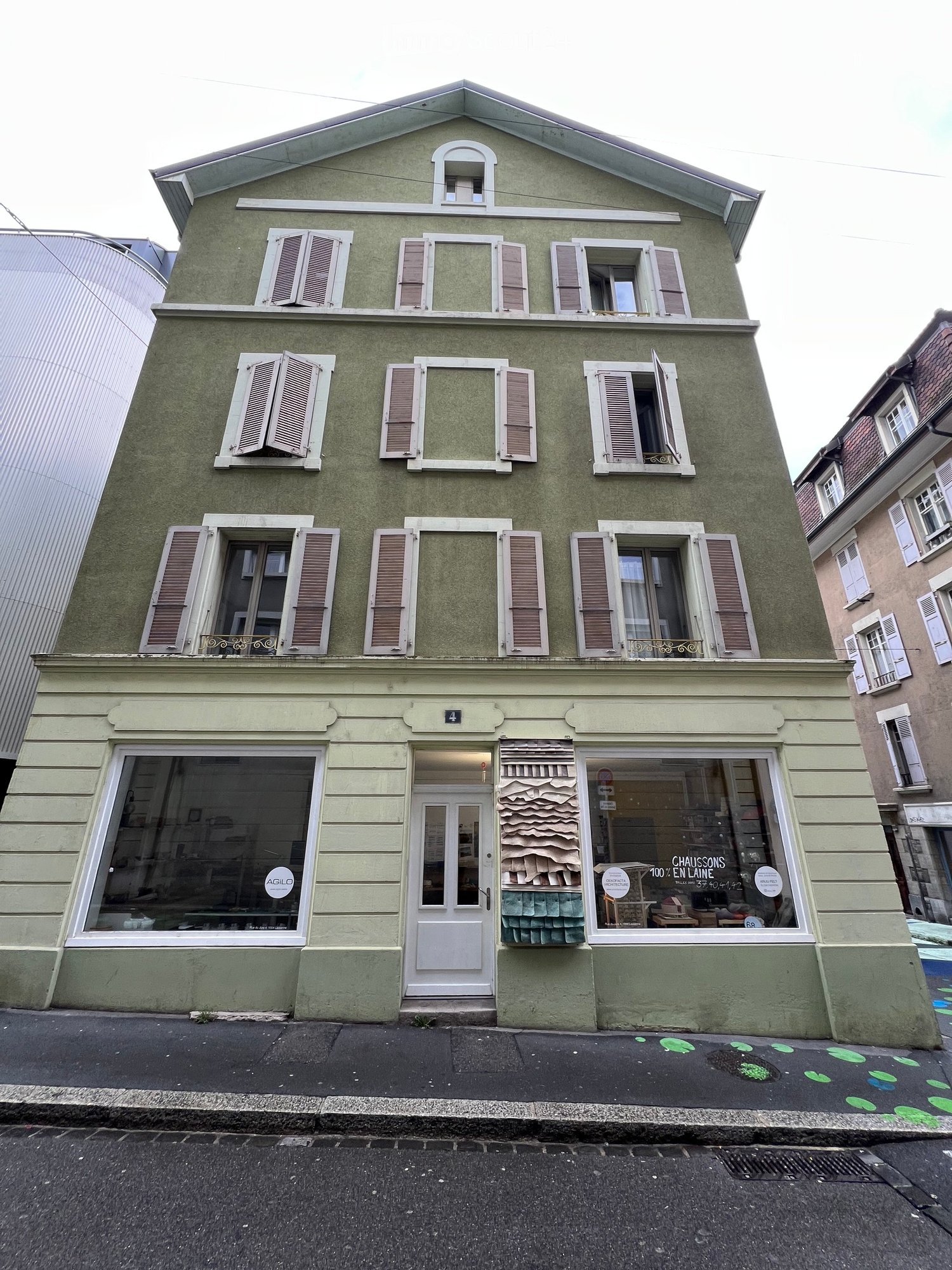 Two-story building with green facade, multiple windows with shutters, and storefronts on the ground floor.