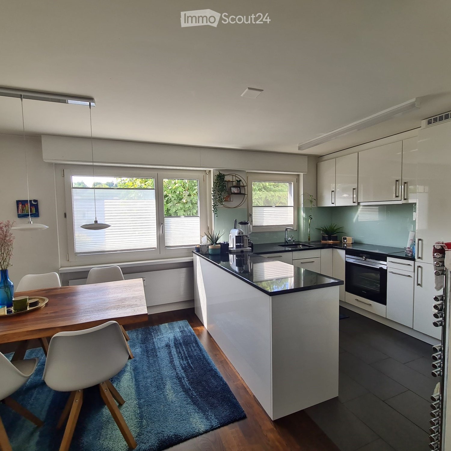 Modern kitchen with white cabinets, black countertops, a dining area with a wooden table and chairs, and a blue rug on the floor.