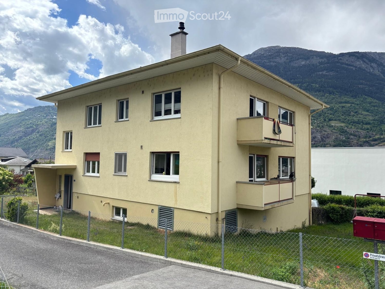 Two-story house with beige exterior, multiple windows, and a balcony overlooking a scenic mountain view.