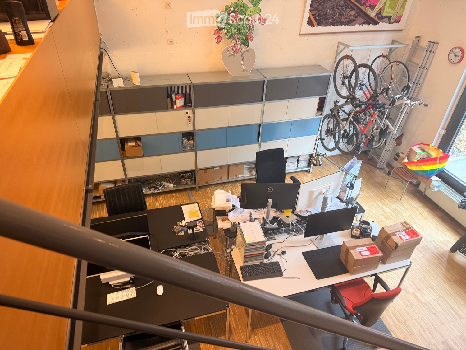 Office space with desks, chairs, computers, shelves, bicycles, and a clock.