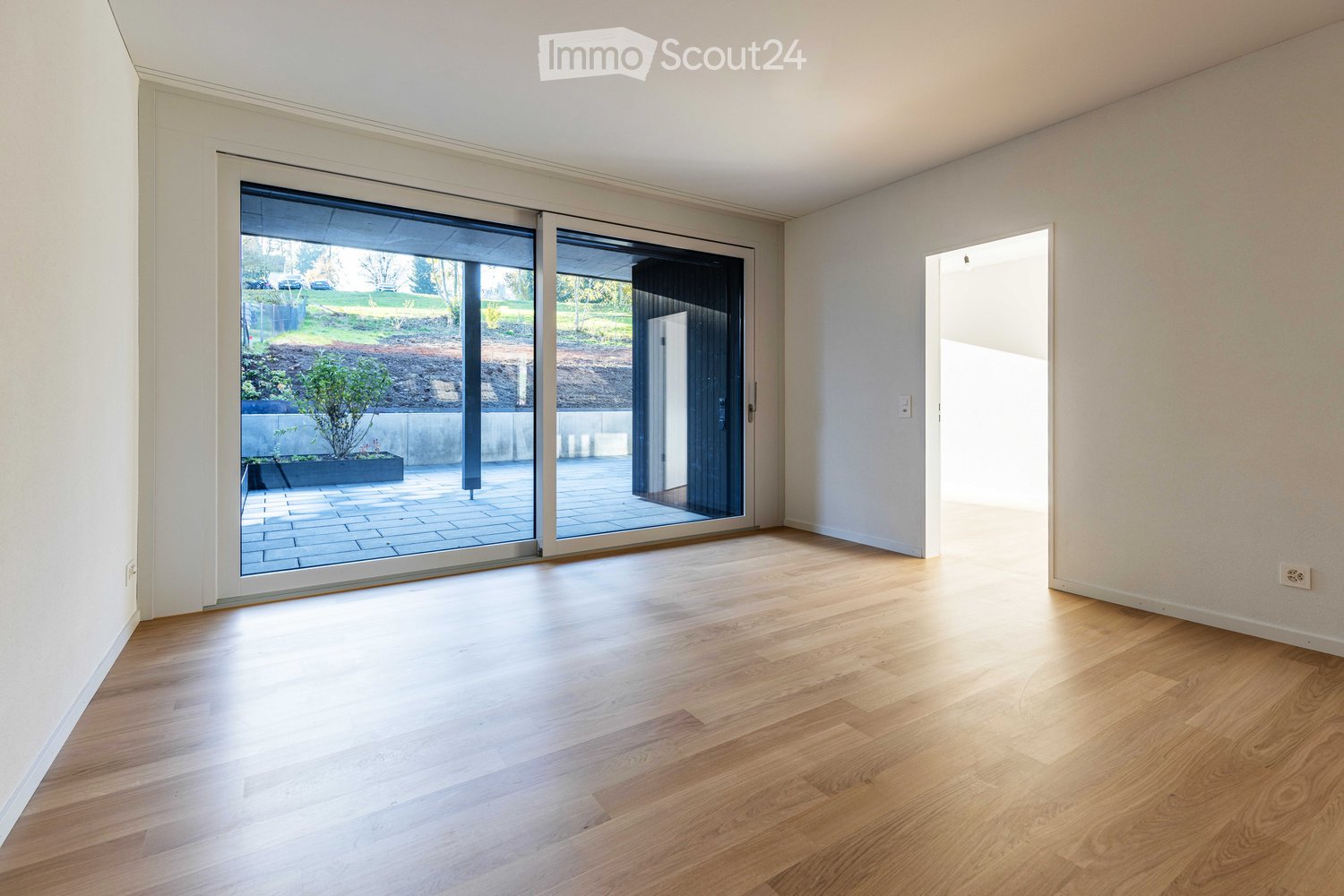Empty room with hardwood floors, white walls, and large sliding glass doors leading to a patio.