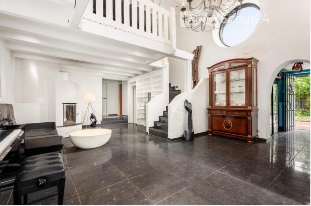 Elegant living room with dark polished tile flooring, white walls, a large wooden cabinet, a grand piano, a white spherical bowl, a sleek black sofa, a floor lamp, and a chandelier.
