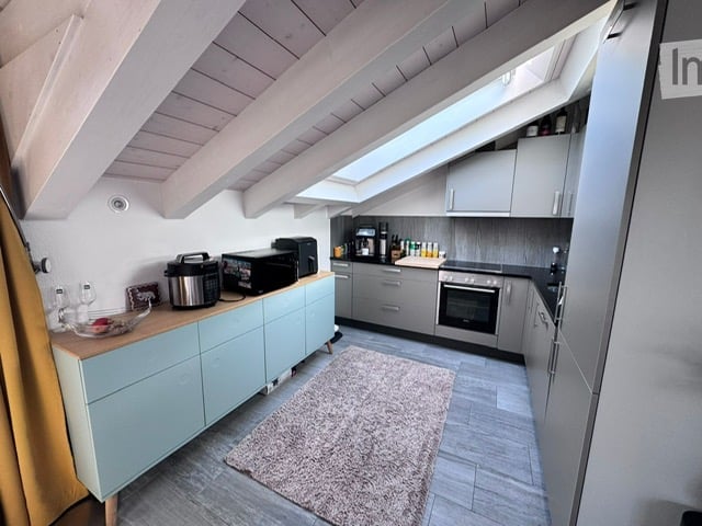 Modern kitchen with light blue cabinets, stainless steel appliances, and a skylight window above the sink. Includes a microwave, coffee maker, toaster, and a small rug on the floor.