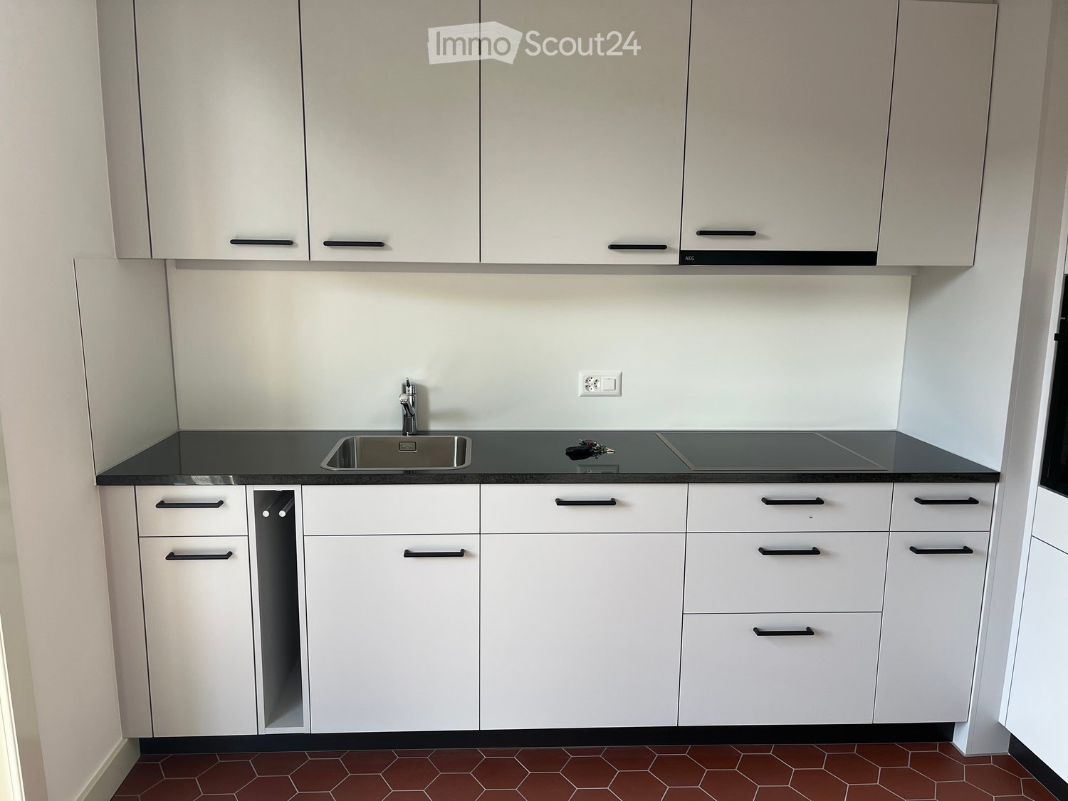 Modern kitchen with white cabinets, black countertop, stainless steel sink, and a faucet. The floor is tiled in a hexagonal pattern.