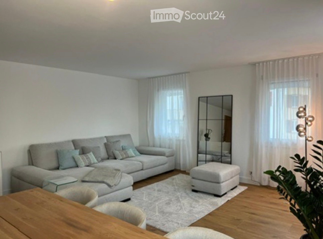 Modern living room with a gray sofa, white rug, and wooden dining table.