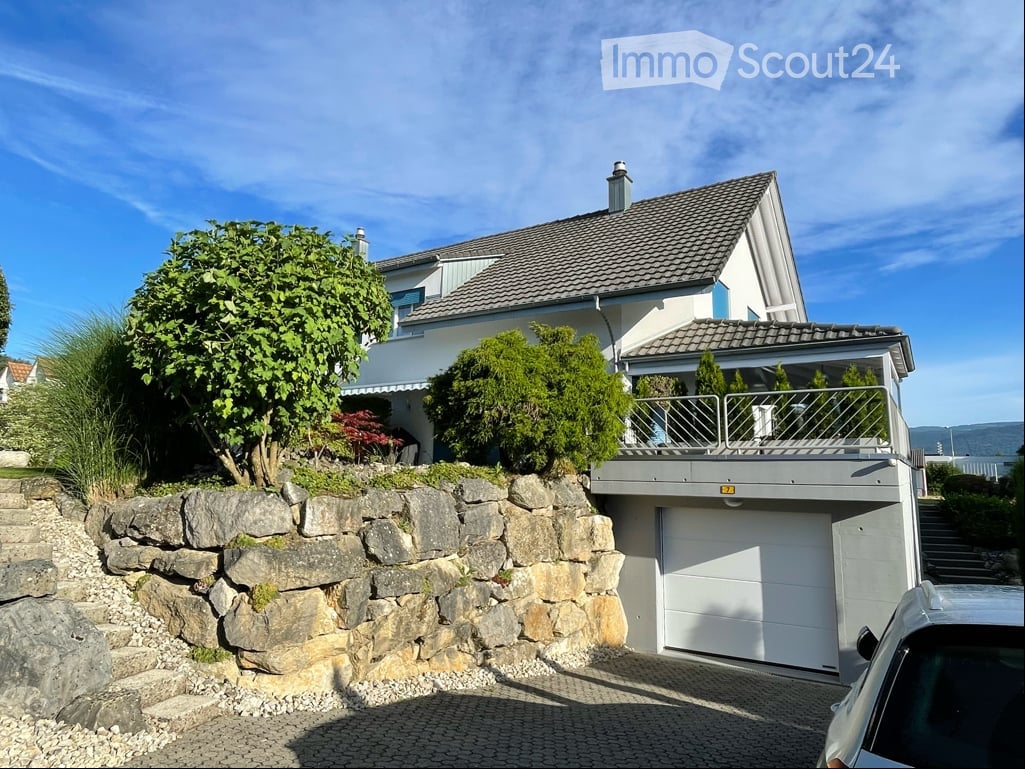 Two-story house with a garage, raised ground floor, and a balcony overlooking the garden.