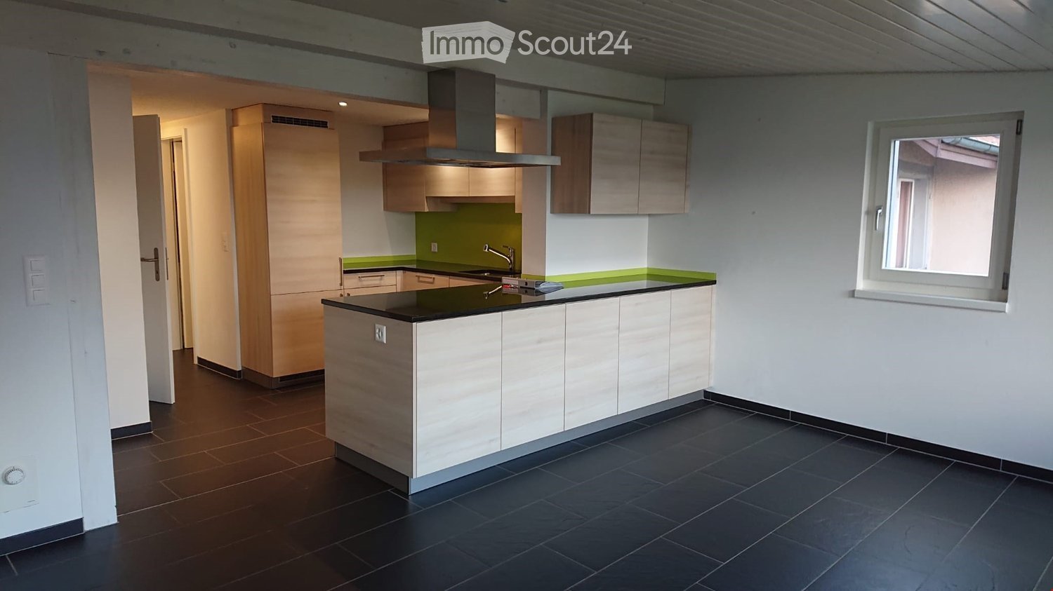 Modern kitchen with white and wood cabinets, black countertop, stainless steel sink, and range hood. Green accent wall and large window.