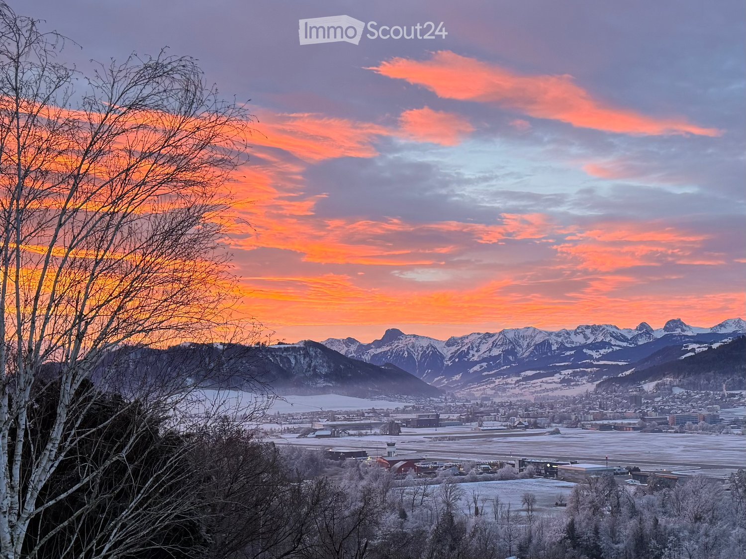 Sunset over mountains, snowy valley, trees, and a town in the distance