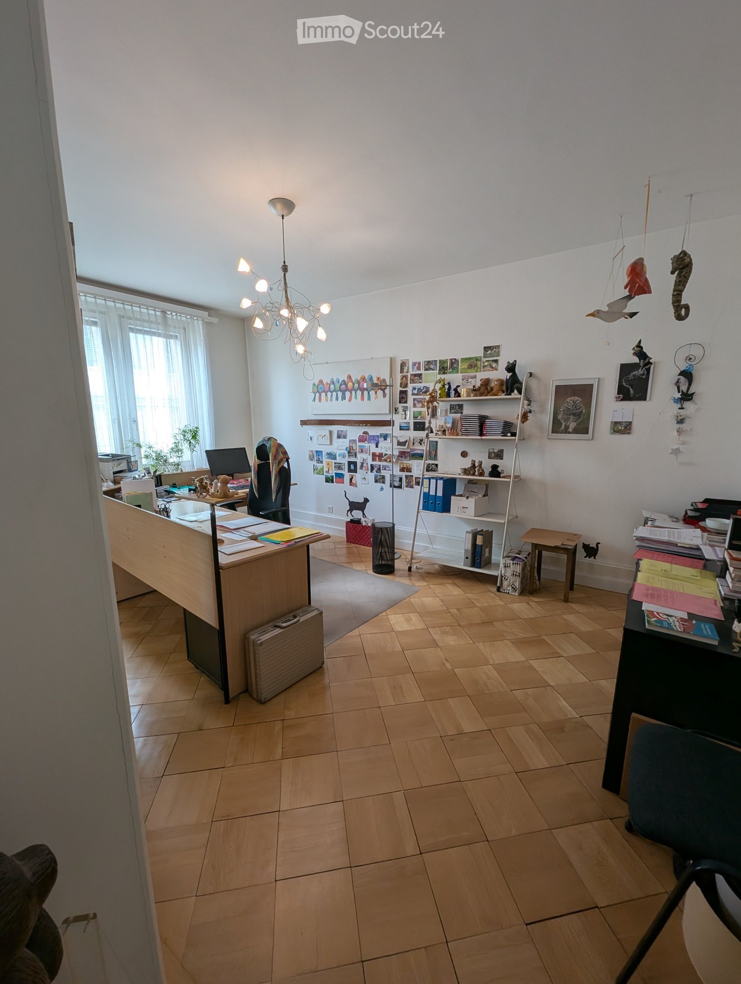 Office space with wooden flooring, large desk, computer, shelves, and decorative items.
