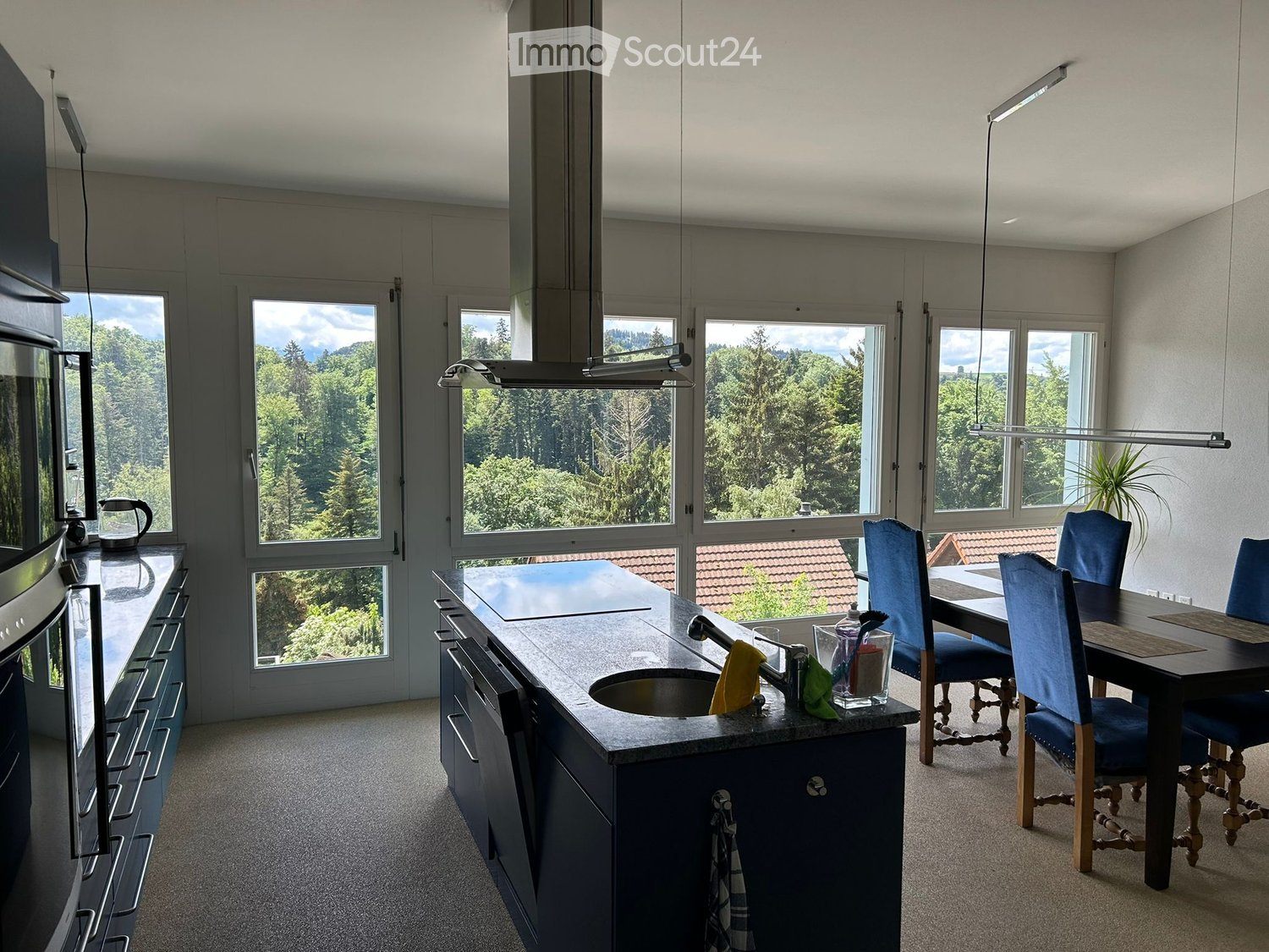 Kitchen. Modern kitchen with large windows offering a scenic view, featuring a central island, sink, oven, and a dining area with a table and chairs.