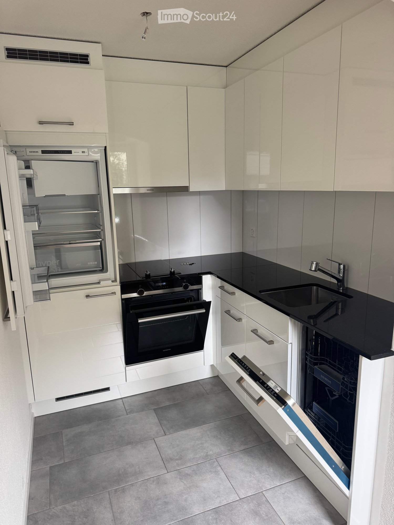 Modern kitchen with white cabinets, stainless steel appliances, black countertops, and grey tiled flooring.