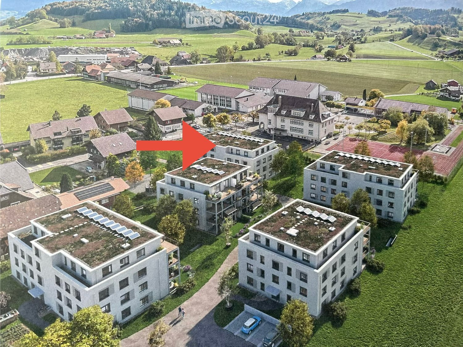 Building. Aerial view of a residential complex with multiple buildings, green roofs, and surrounding landscape with fields and trees.