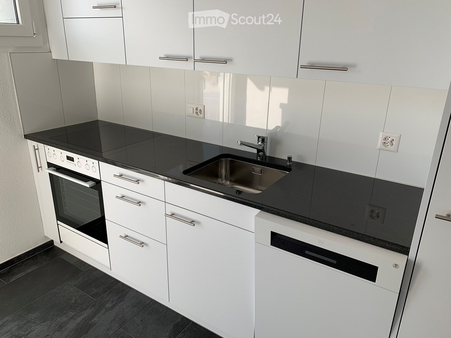Modern kitchen with white cabinets, black countertops, stainless steel sink, and built-in oven.