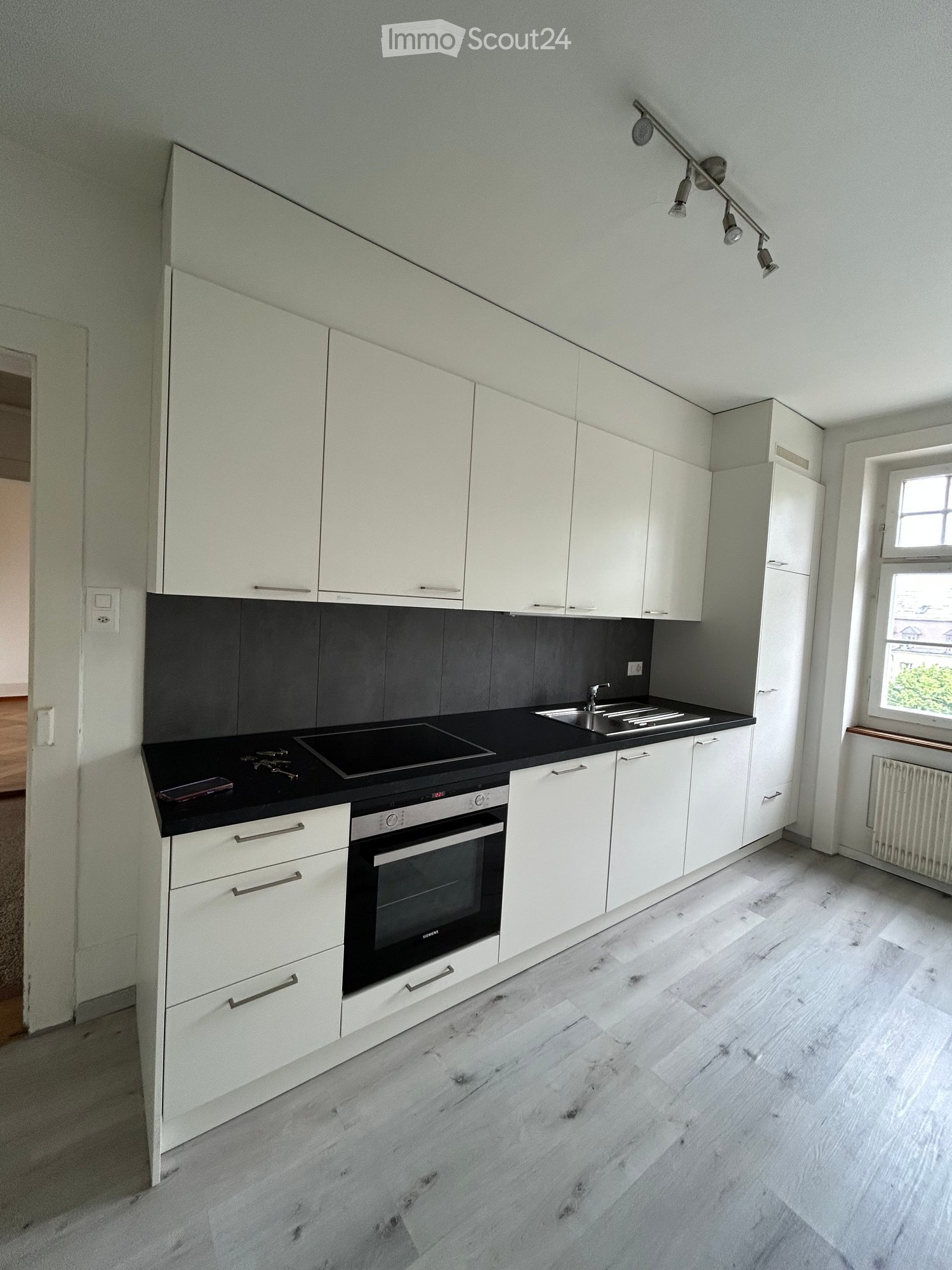 Modern kitchen with white cabinets, black countertops, and a built-in oven. Features a sink, faucet, and a sleek light fixture above the counter.