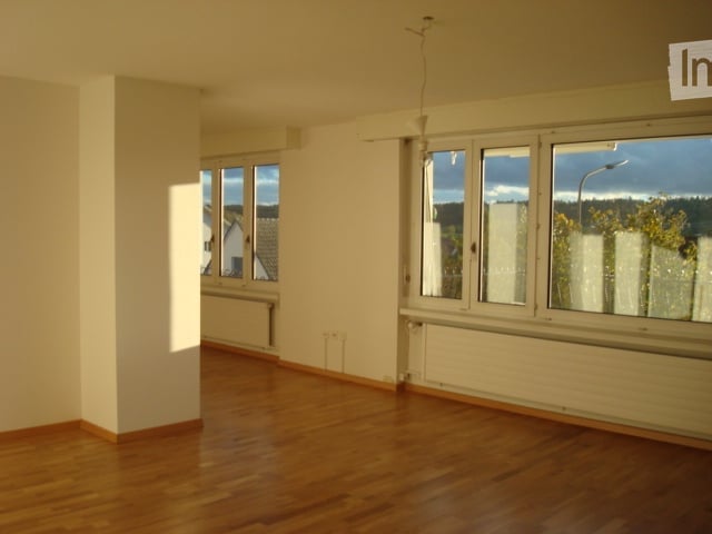 Empty room with wooden flooring, white walls, and large windows with a view of the outside. No furniture or equipment present.