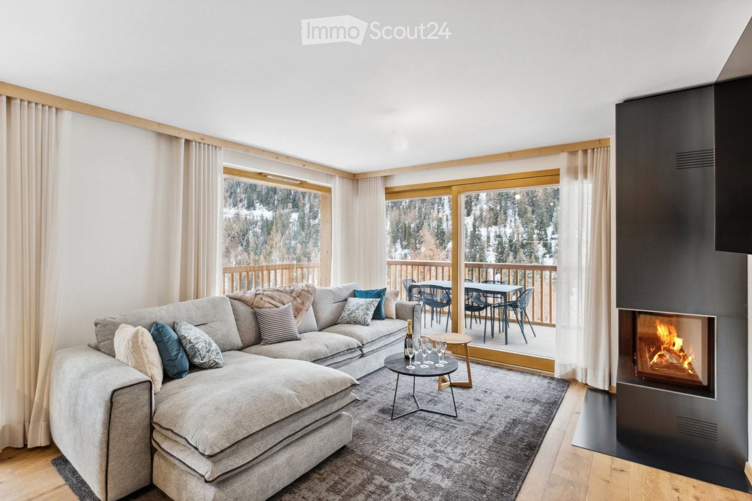Modern living room with a large sectional sofa, fireplace, coffee table, and large windows offering a scenic view of a snowy landscape.