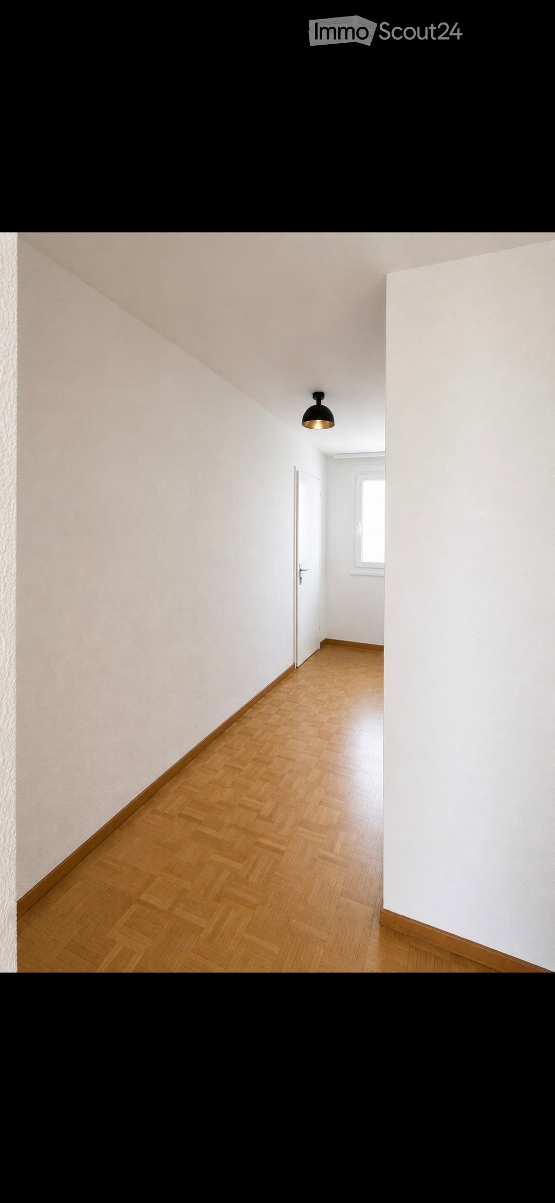 Empty hallway with wooden flooring, white walls, and a single light fixture. No furniture or equipment is present.