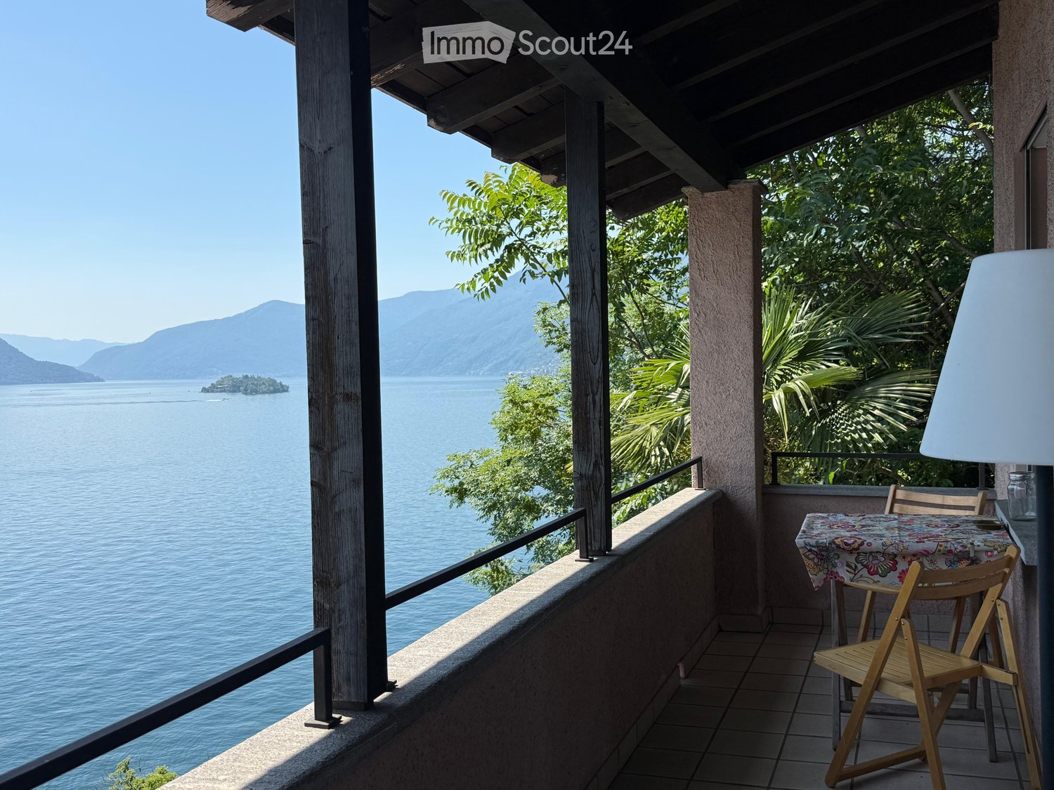 Balcony with a scenic lake view, featuring a table and chairs, surrounded by lush greenery and a wooden ceiling.