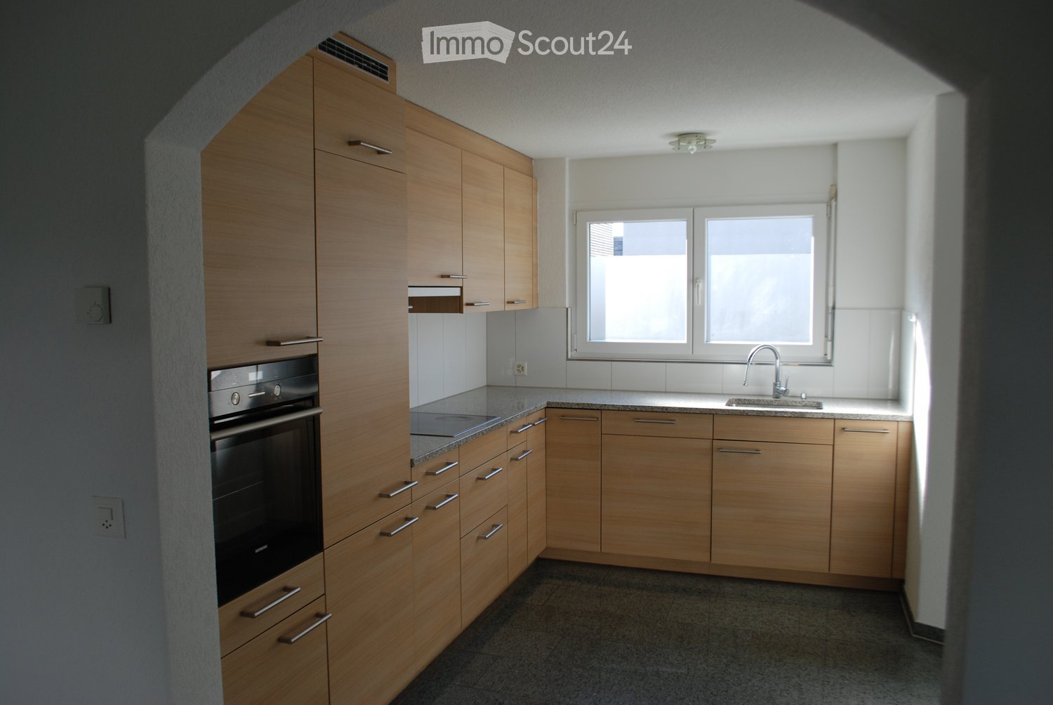 Modern kitchen with light wooden cabinets, stainless steel oven, granite countertop, and a window above the sink.