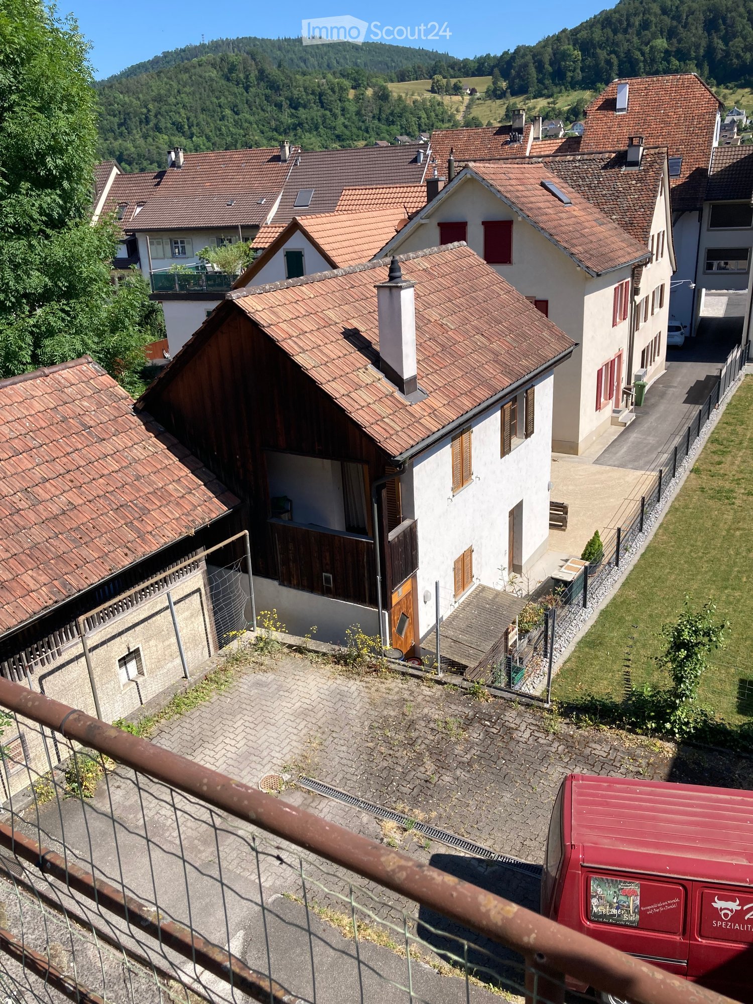 Aerial view of a residential area with multiple houses featuring red-tiled roofs, surrounded by greenery and hills in the background.