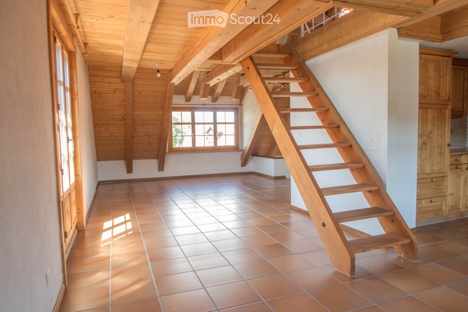 Bright hallway with wooden staircase, exposed wooden beams, tiled floor, and large windows allowing natural light.