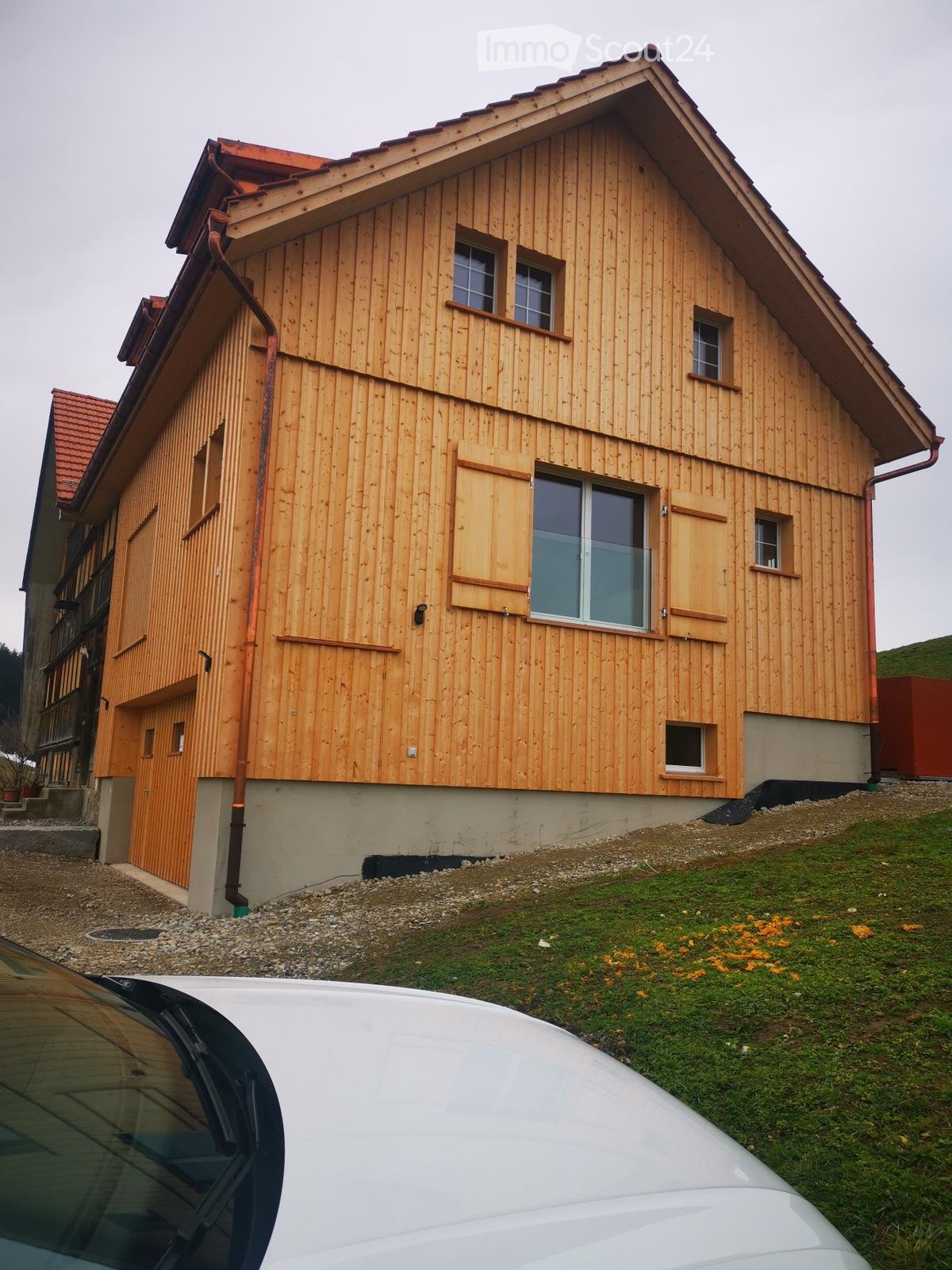 Wooden exterior, 3 windows, garage, red roof, gravel driveway